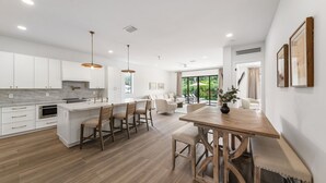 Une cuisine moderne avec des meubles blancs, un îlot central doté de tabourets de bar et un coin repas avec une table et des chaises en bois.