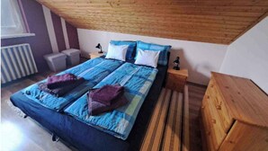 Une chambre avec un plafond en pente, un lit double avec une literie bleue et blanche, une table de chevet en bois et un radiateur.