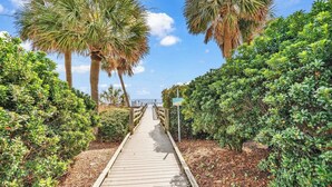 Un sentier en bois menant à une plage, bordé d’une végétation luxuriante et de palmiers.