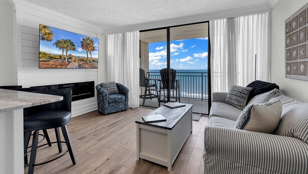 Un salon moderne avec vue sur l’océan, un coin repas et un balcon équipé d’une chaise.