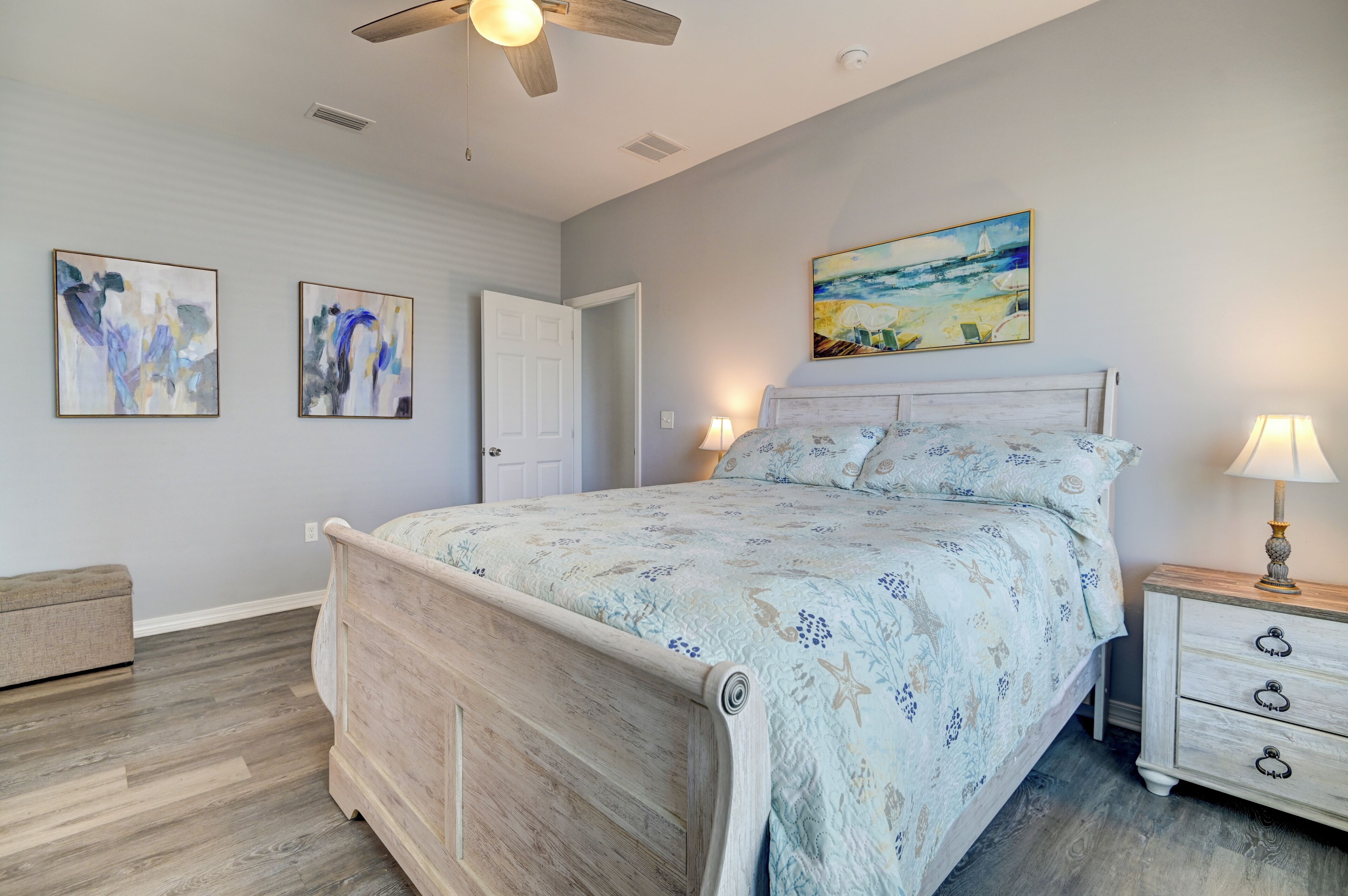 A bedroom with a bed, nightstands, a dresser, a ceiling fan, and artwork on the walls.