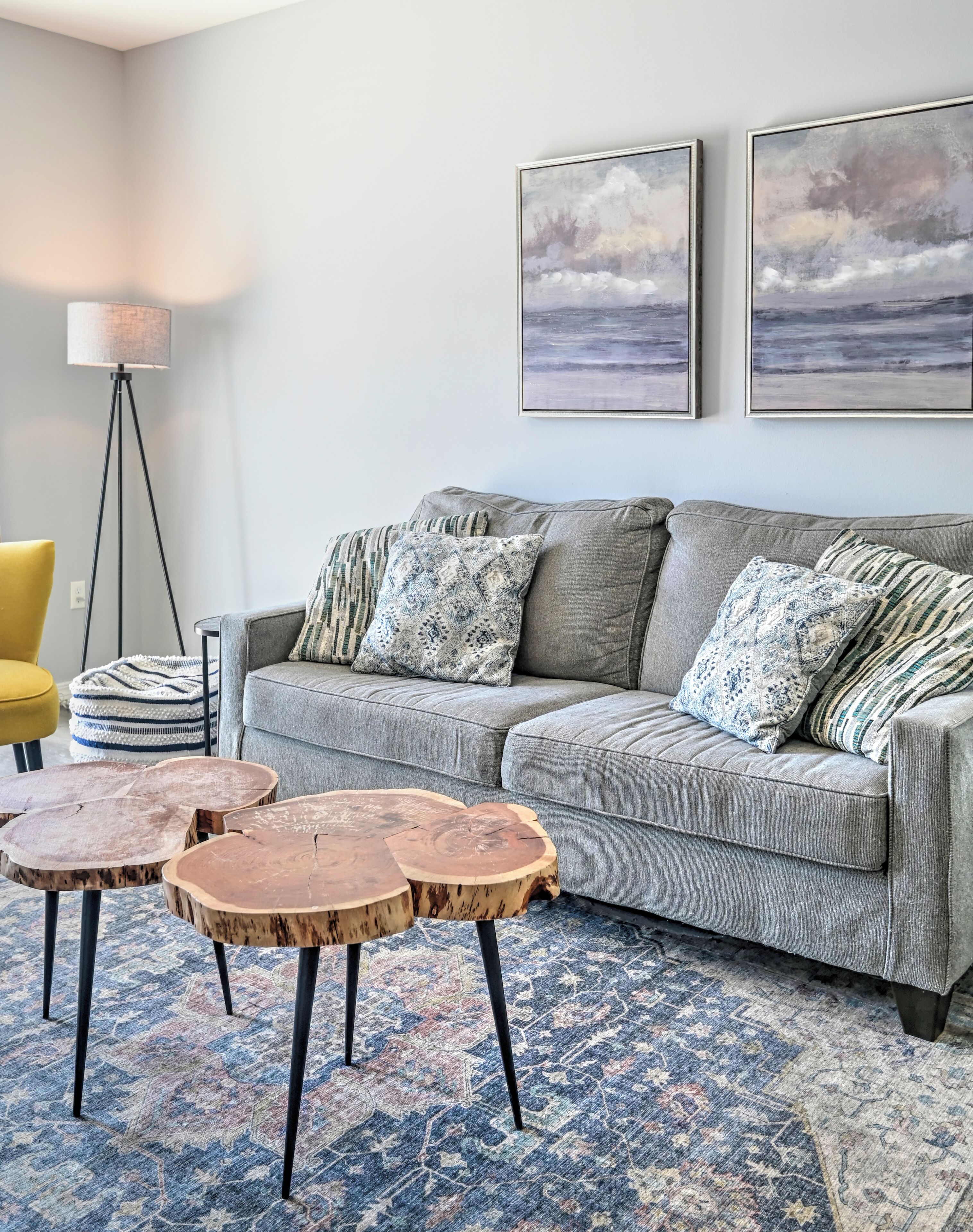 Un salon avec un canapé gris, des coussins à motifs, un tapis bleu et beige, et un lampadaire.