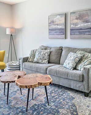 Un soggiorno con un divano grigio, cuscini decorati, un tappeto blu e beige e una lampada da terra.