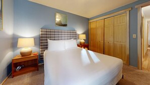 Hotellihuone, jossa on suuri sänky, kaksi yöpöytää valaisimineen, ruutukuviollinen pääty, puinen vaatekaappi ja seinällä oleva kehystetty kuva.