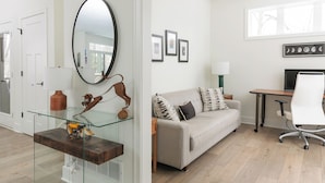 Un salon moderne avec une table basse en verre, un canapé agrémenté de coussins à motifs, un bureau avec une chaise et des tableaux encadrés accrochés au mur.