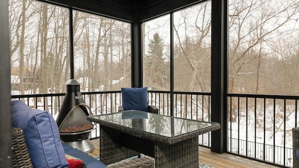 Un espace extérieur abrité, aménagé avec des meubles en osier, une table à plateau en verre et un barbecue.