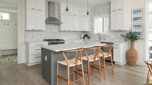 Une cuisine moderne avec des meubles blancs, un grand îlot central doté de tabourets, un éclairage suspendu et une grande fenêtre.