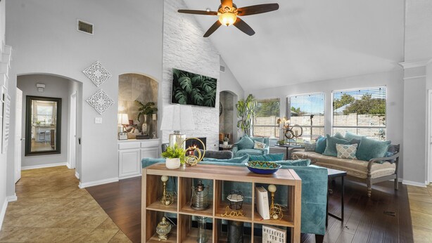 Un salon spacieux avec un plafond haut, un meuble de rangement en bois pour les appareils multimédias, une grande fenêtre avec des stores et un coin salon confortable avec un canapé et des fauteuils.