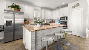 Une cuisine moderne avec des meubles blancs, des appareils en acier inoxydable, un plan de travail en granit et un îlot central doté de tabourets de bar.