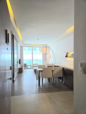 A modern hotel room with a dining area, a kitchen, and a large window providing natural light. - A La Carte Da Nang 2-bedroom Sea View Apartment - Beach Front (Đà Nẵng)