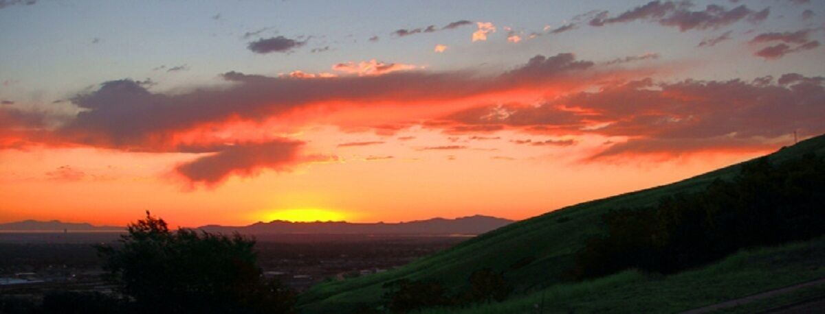 A sunset over a hilly landscape with a clear sky.