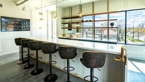 Een moderne bar met barstoelen, een glazen displayplank en een groot raam met uitzicht op buiten.