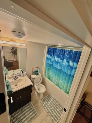 A bathroom with a bathtub, toilet, sink, and a mirror. - Modern Basement Suite w/ Free Parking & Trails (Winnipeg)