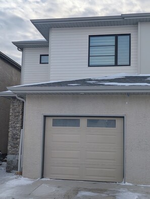 A two-story house with a garage and a small window on the upper floor. - Modern Basement Suite w/ Free Parking & Trails (Winnipeg)
