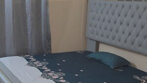 A bed with a tufted headboard, a floral-patterned bedspread, and a grey curtain.