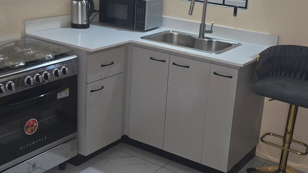 A compact kitchen with white cabinets, a gas stove, a microwave, and a sink.
