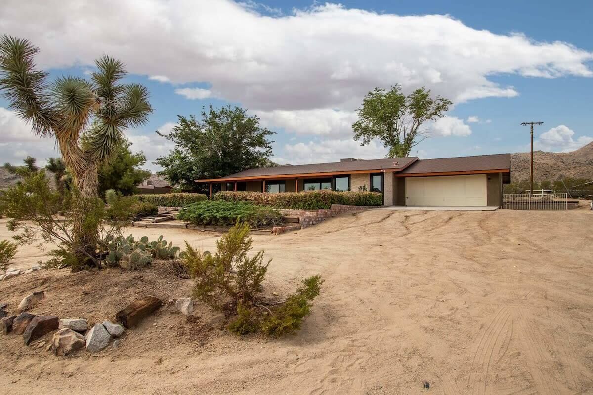 A modern house with a garage, surrounded by desert vegetation and a clear sky.