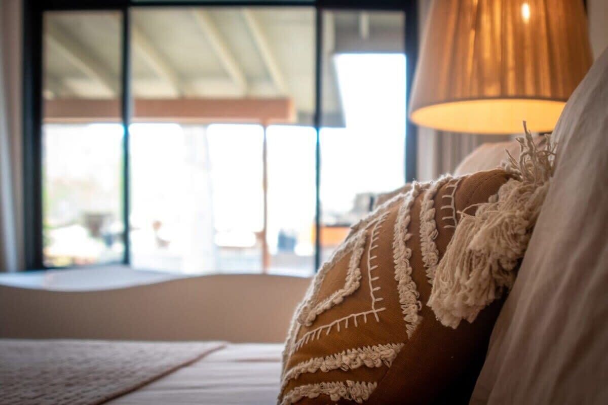 Une pièce confortable avec une grande fenêtre, un coussin moelleux de couleur marron orné d’une bordure blanche et une lampe chaleureuse.