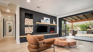 A modern living room with a fireplace, a round wooden table, and a comfortable armchair. - Marbella Lane - The Wine Mine Desert Escape (Joshua Tree)