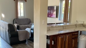 A spacious living area with a grey sofa, a wooden cabinet, and a tiled floor. - Hidden Treasure Vacation Home (Caye Caulker)