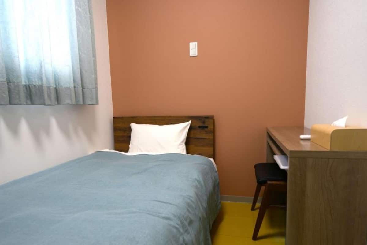 Una cama individual con cabecera de madera, un escritorio con silla y una mesita de noche con lámpara.