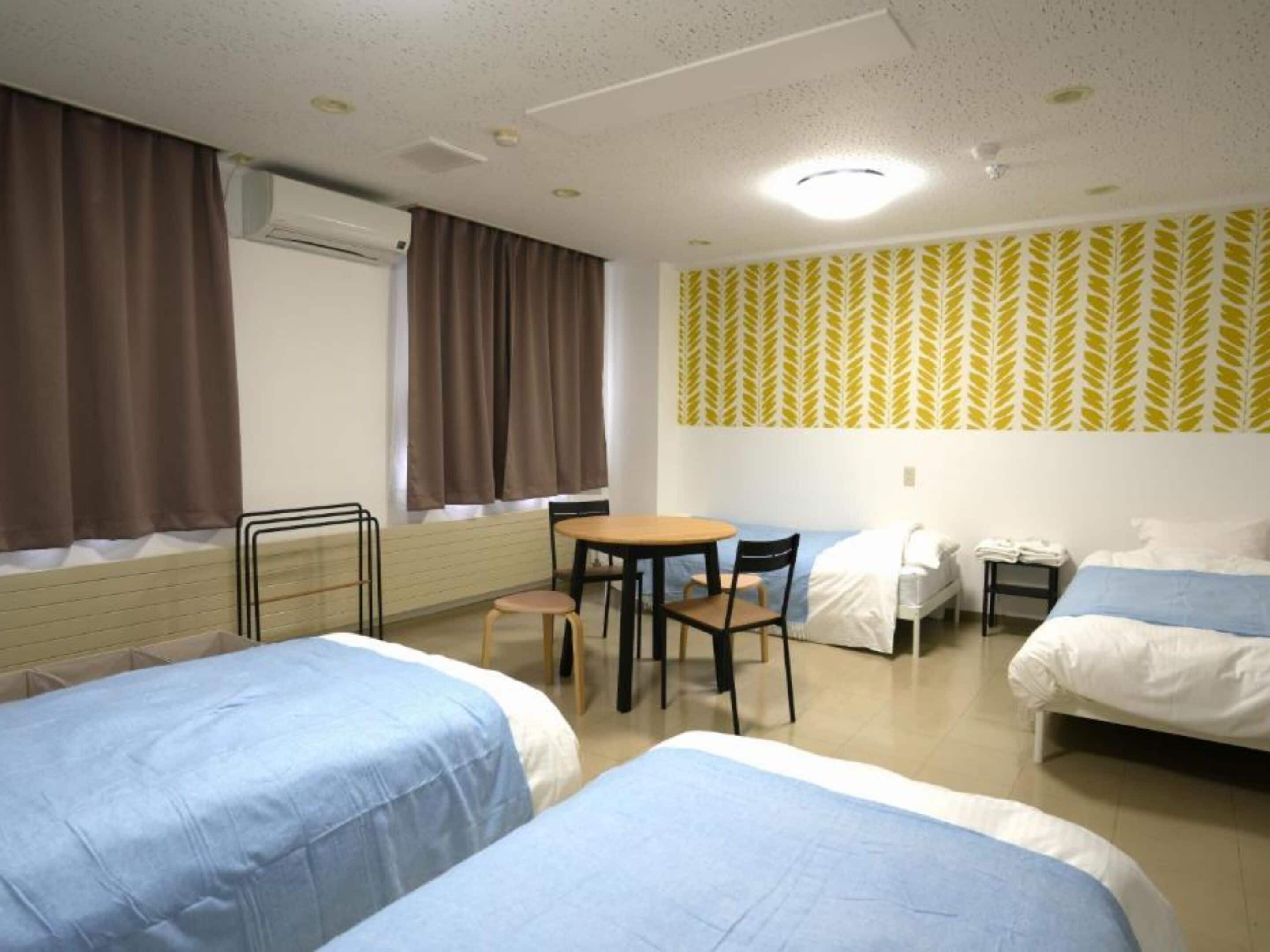 Ein Hotelzimmer mit zwei Betten, einem kleinen Tisch, Stühlen, einem Schreibtisch und einem Fenster mit Vorhängen.