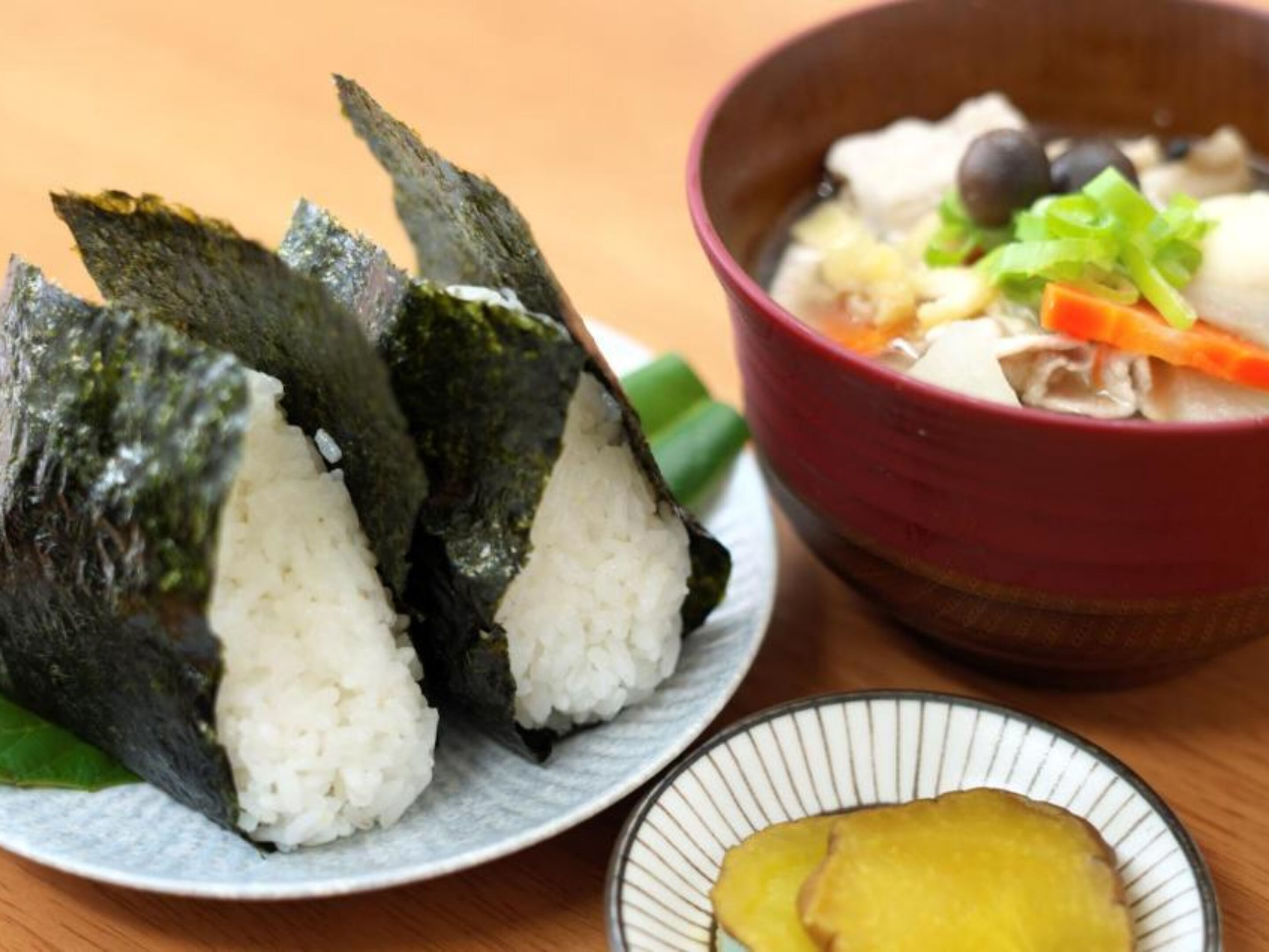 Une assiette de makis (rouleaux de sushi) au riz et aux algues, un bol de soupe aux légumes et une petite portion de gingembre mariné.