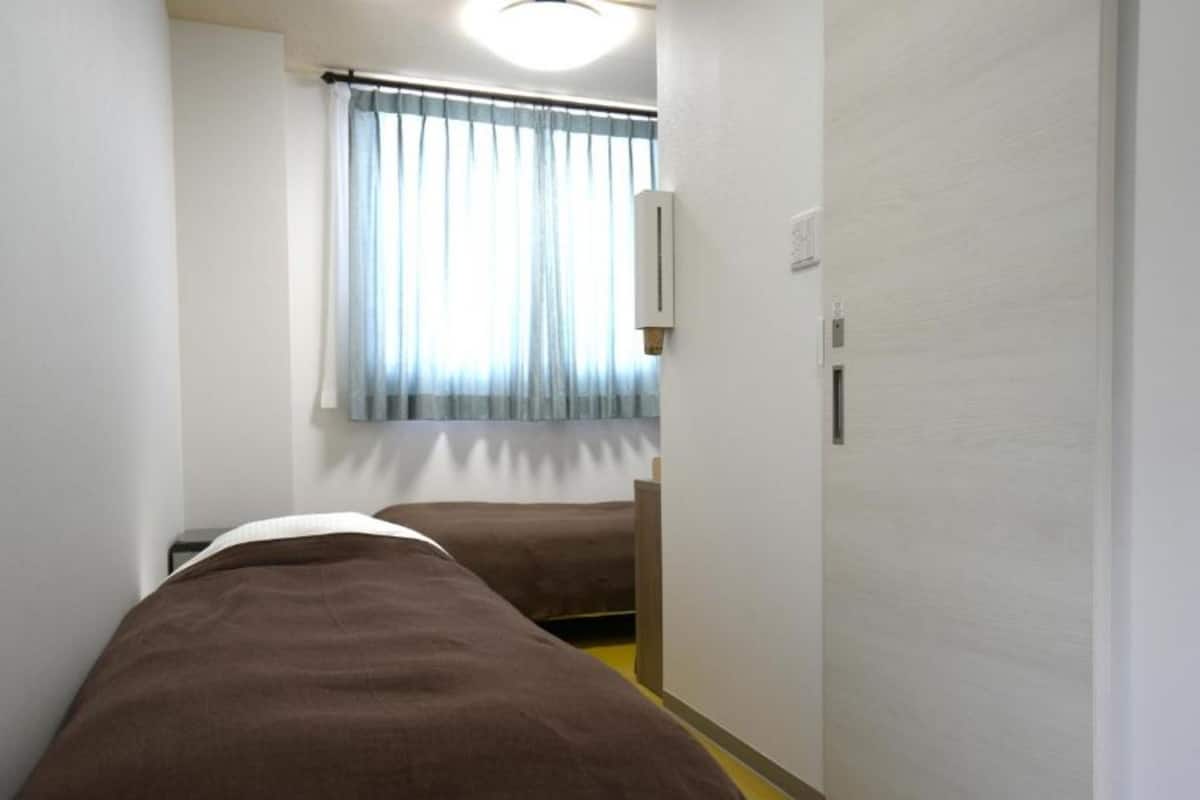 Un pasillo estrecho con dos camas, una ventana con cortinas y una puerta.