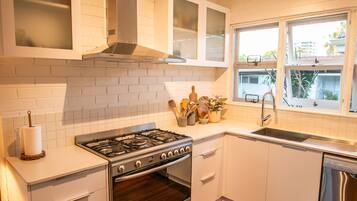 A kitchen with white cabinetry, a stainless steel stove, and a window with a view of the outside.