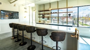 Ett modernt barområde med barstolar, en hylla i glas för att visa upp varor och ett stort fönster med utsikt över omgivningen.
