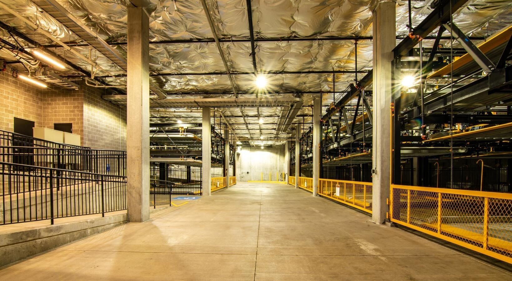 An indoor parking garage with concrete floors, metal railings, and exposed ductwork.