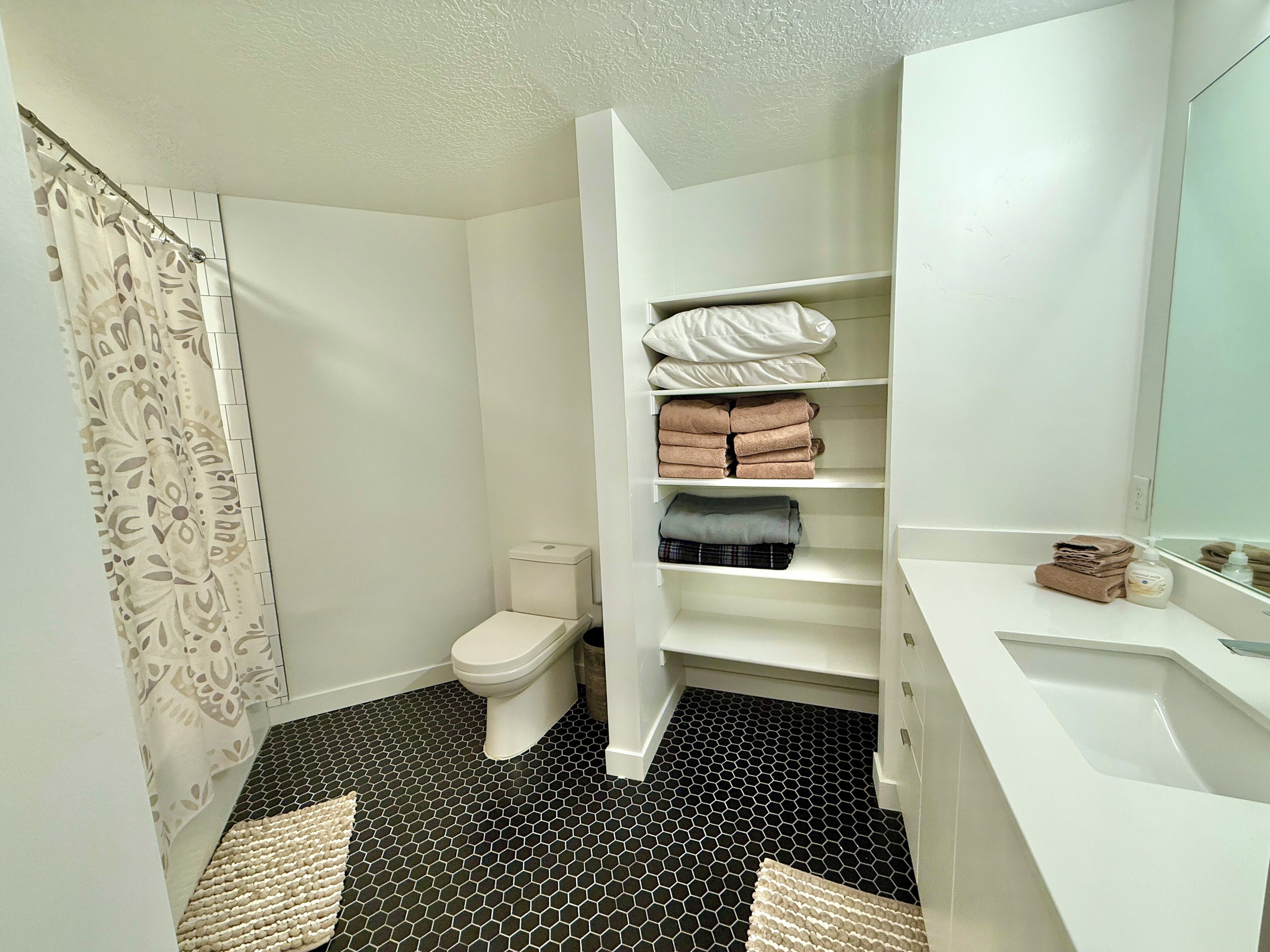 A bathroom with a toilet, a shower curtain, a sink, and a storage cabinet with towels.