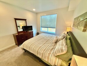 Een slaapkamer met een bed, een dressoir, een televisie, een raam en kunst aan de muur.