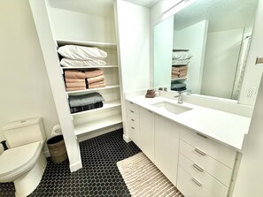 Een badkamer met toilet, een wastafel, een spiegel en planken met opgevouwen handdoeken.