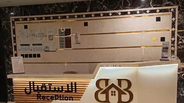 Un mostrador de recepción con piso de mármol, diseño de paneles de madera y un logotipo con escritura árabe.