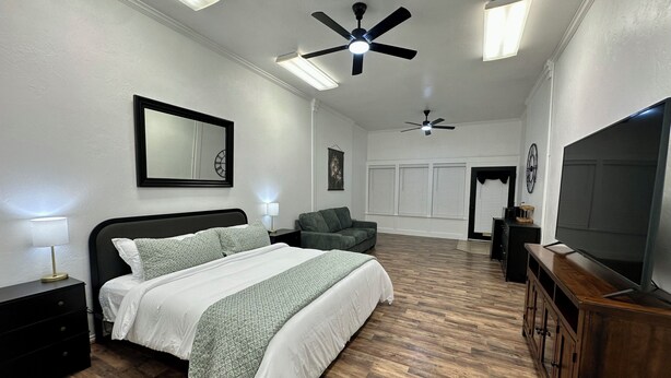 A bedroom with a bed, a TV, a ceiling fan, and a large window.