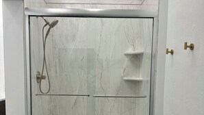 A glass-enclosed shower with a marble wall, a towel rack, and a door with a brass handle.