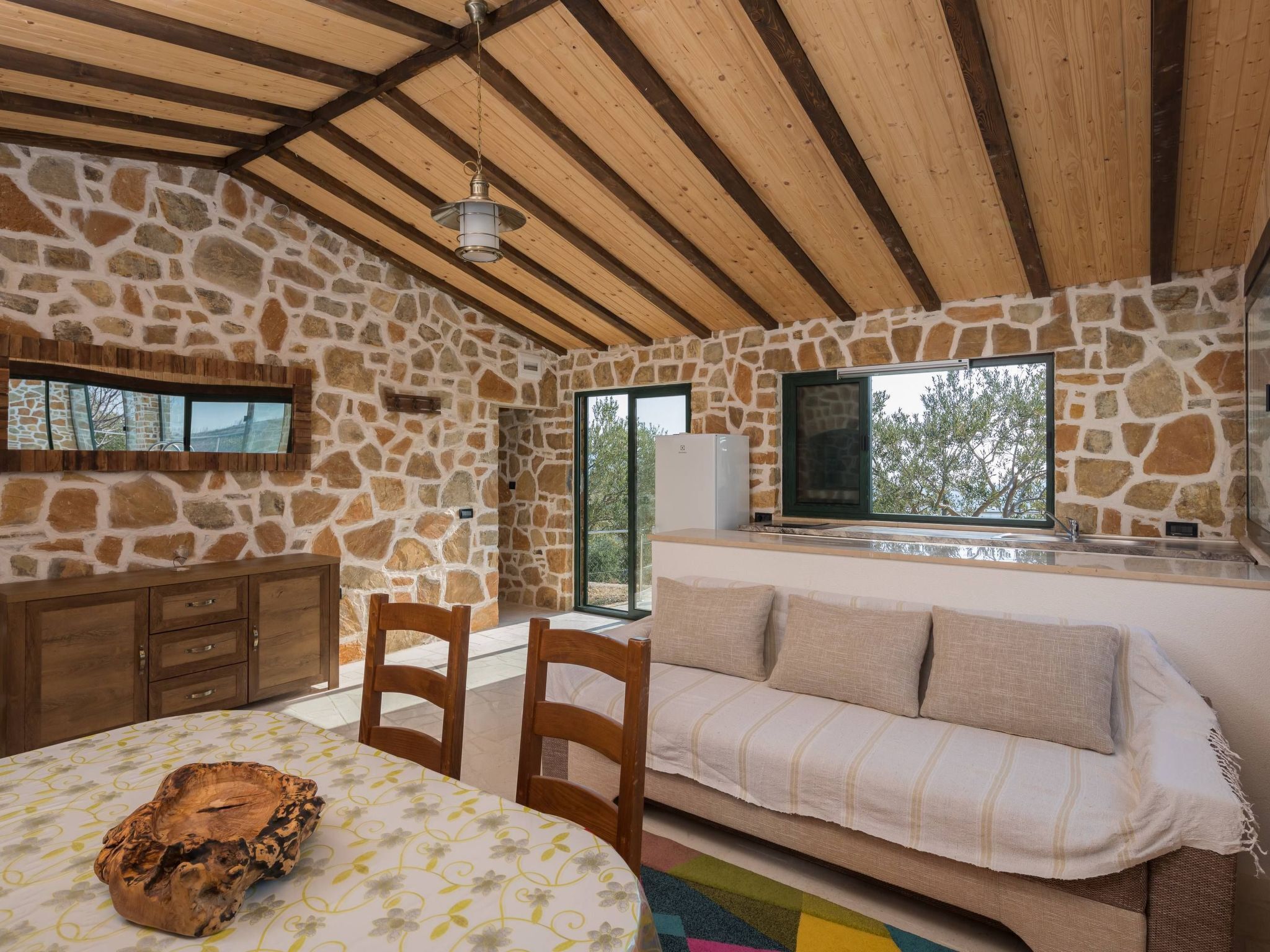Une pièce rustique aux murs de pierre, avec un plafond en bois, un canapé, une table à manger et une cheminée en pierre.