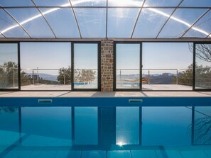 En modern inomhuspool med stora glasdörrar och utsikt över det omgivande landskapet.