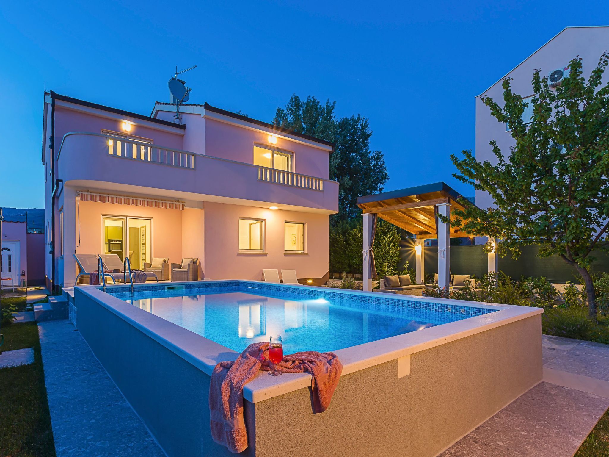 Uma casa de dois andares com piscina, área de estar ao ar livre e varanda coberta.