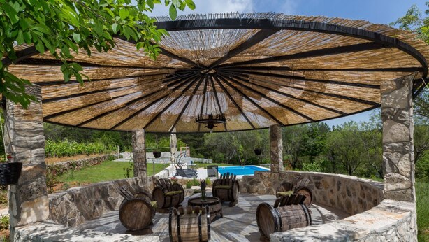 Ein Außenbereich mit Steinmauern, Holzfässern, einem Pool und einer Pergola mit einem gewebten Dach.