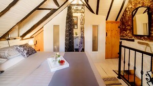 A bedroom with a sloped ceiling, a bed with a tray of fruit and a glass, a wooden door, and a mirror on the wall.