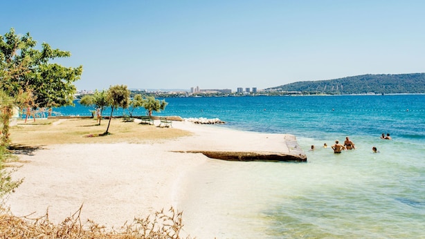 A beach with clear blue water, a sandy shore, and a few people swimming.