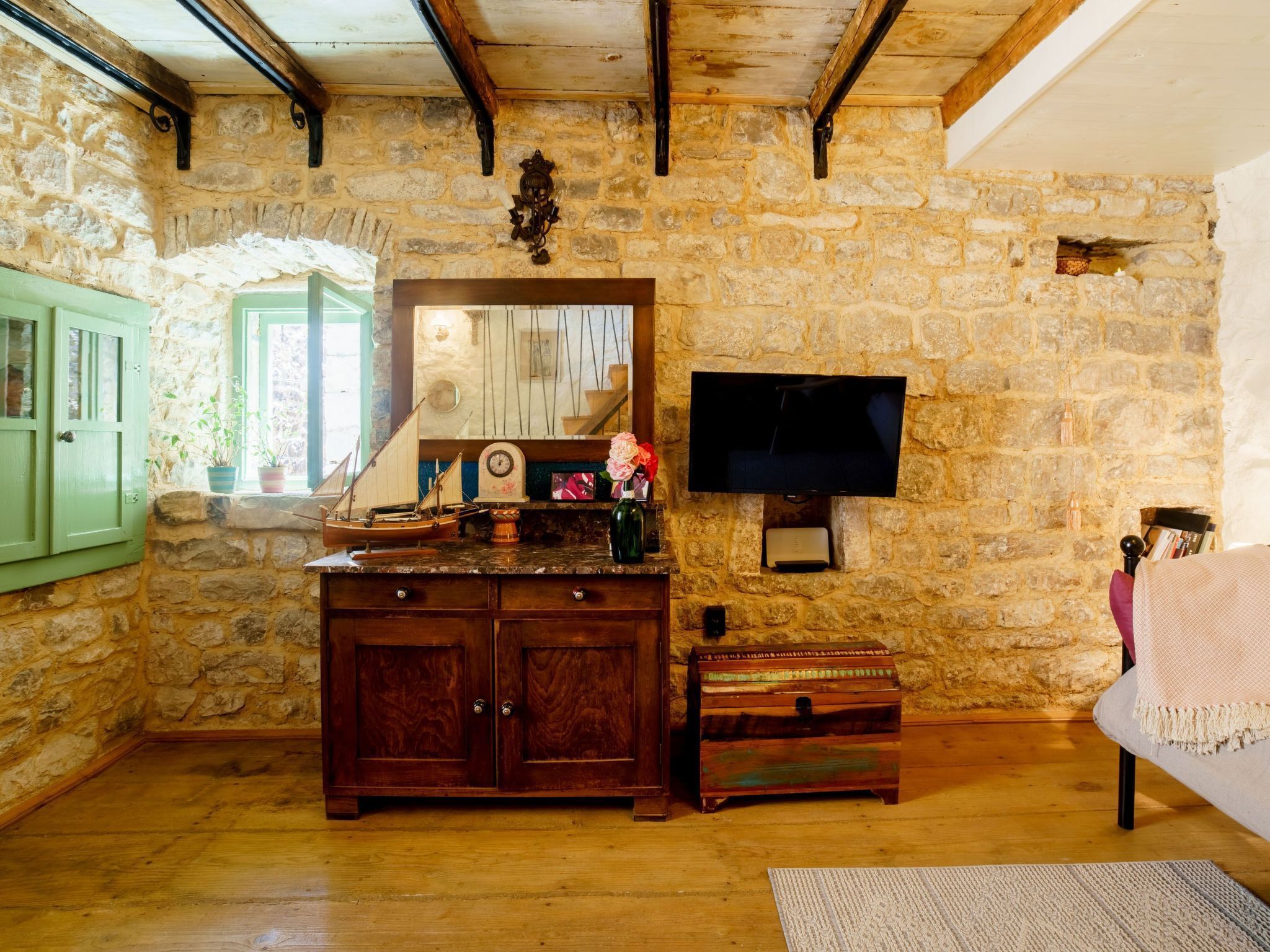 A rustic room with stone walls, wooden beams, a wooden cabinet, a television, and a cozy seating area.