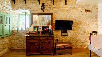 A rustic room with stone walls, wooden beams, a wooden cabinet, a television, and a cozy seating area.
