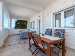 Varanda espaçosa com mesa e cadeiras de jantar, um sofá e um vaso com planta.