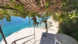 A beach with a thatched roof structure, a table, and a chair. - "Carmen" mit Whirlpool by Interhome (Vinišće)