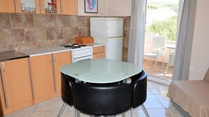 Una cocina compacta con estufa a gas, refrigerador y comedor con mesa de vidrio y sillas.