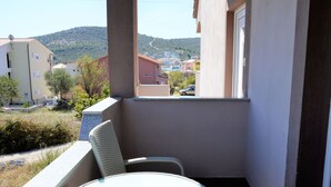 Un balcón con mesa y silla, con vista a una zona residencial y colinas.