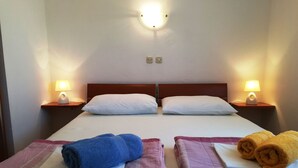 Ein Hotelzimmer mit zwei Betten, jedes mit einem Kopfkissen und einem gerollten Handtuch. An beiden Seiten der Betten stehen Nachttischlampen.